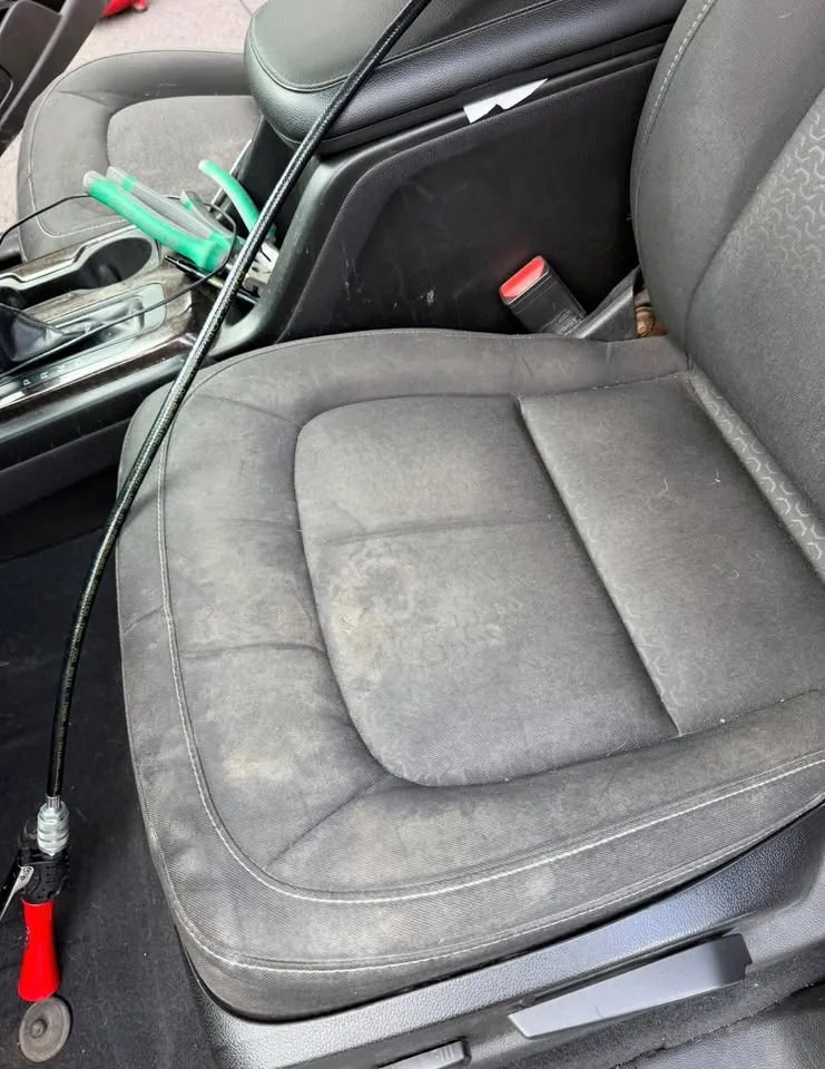 A stained black cloth seat with an extractor hose across it, before cleaning