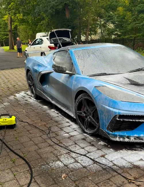 A blue Corvette covered in foam on a paved driveway