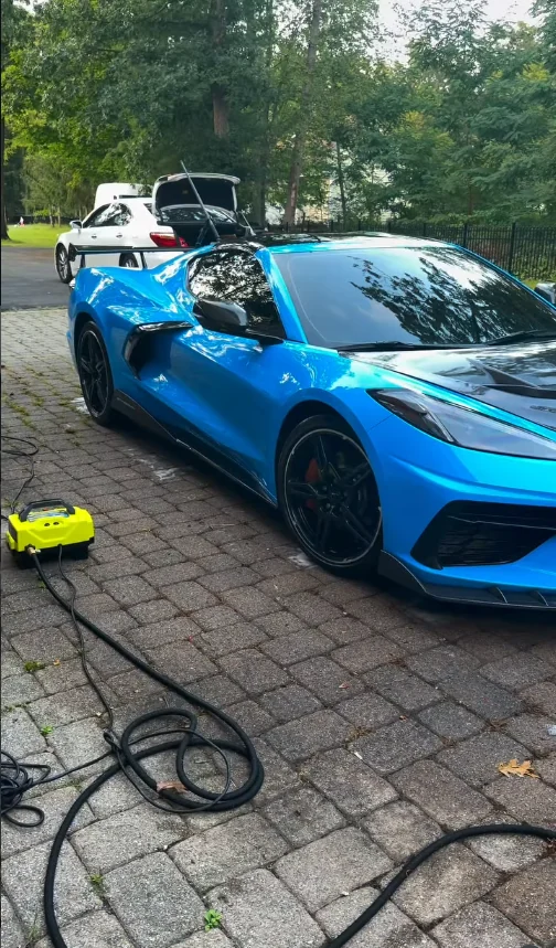 A blue Corvette with its panels open, being detailed in a driveway