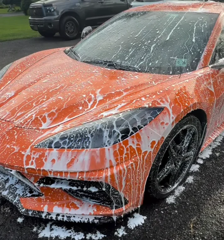 An orange Corvette covered in snow foam during an exterior detail