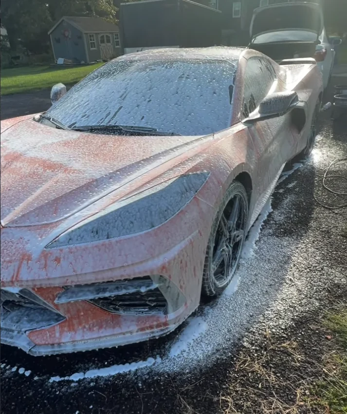 The front of an orange Corvette under a layer of snow foam